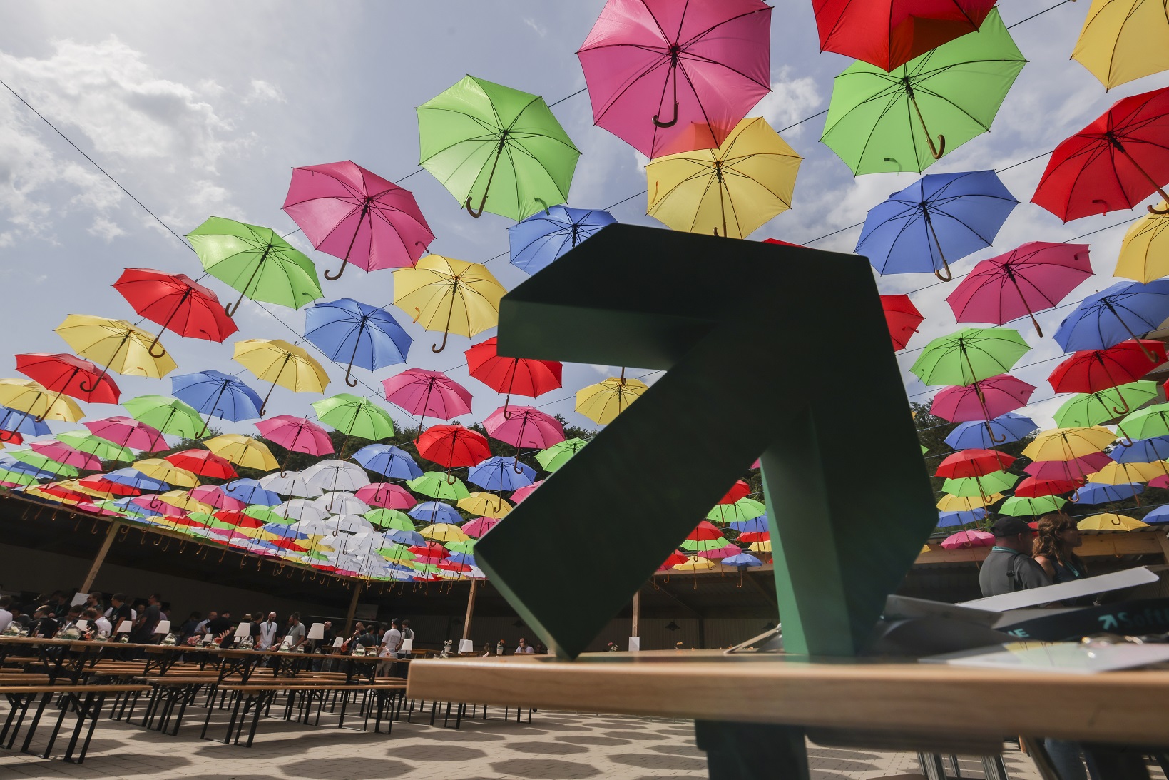 Der SoftENGINE Logo Pfeil steht auf einer Bank, im Hintergrund hängen viele bunte Regenschirme